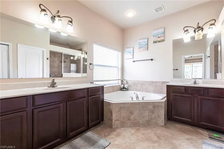 Bathroom featuring a bath, visible vents, a stall shower, two vanities, and a sink