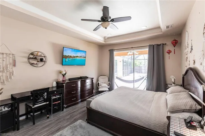 Bedroom with access to outside, a ceiling fan, wood finished floors, a tray ceiling, and visible vents