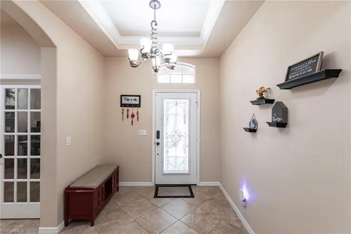 Entryway with arched walkways, light tile patterned floors, a raised ceiling, a notable chandelier, and ornamental molding