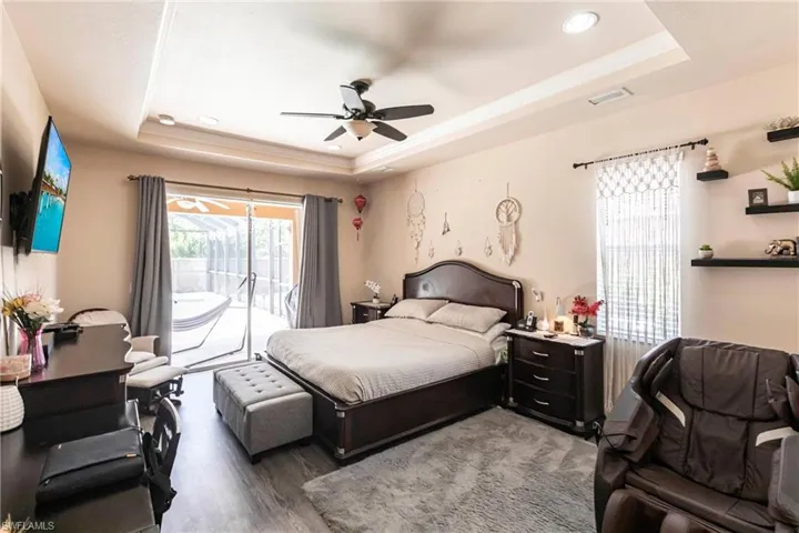 Bedroom with a ceiling fan, visible vents, access to exterior, wood finished floors, and a raised ceiling