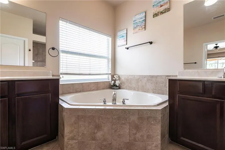 Full bathroom with visible vents, tile patterned flooring, a bath, and two vanities