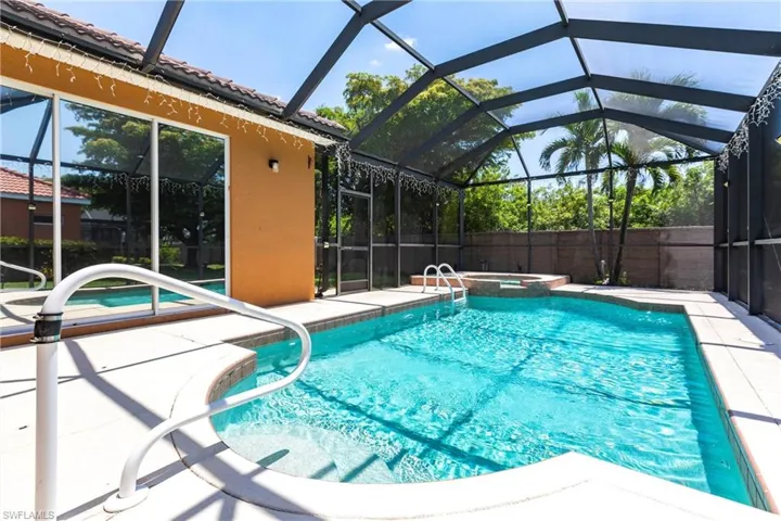 View of swimming pool featuring glass enclosure, a patio, and a pool with connected hot tub