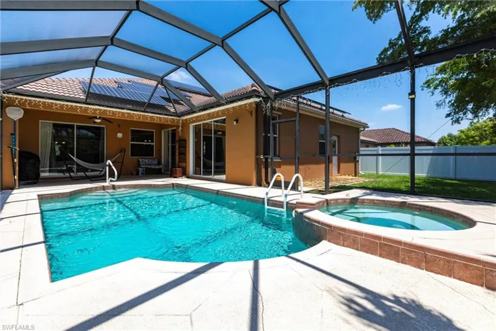 View of pool with fence, a pool with connected hot tub, a lanai, a ceiling fan, and a patio