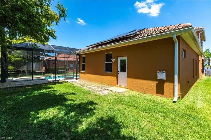 Rear view of property featuring a tile roof, a lawn, central AC, roof mounted solar panels, and stucco siding