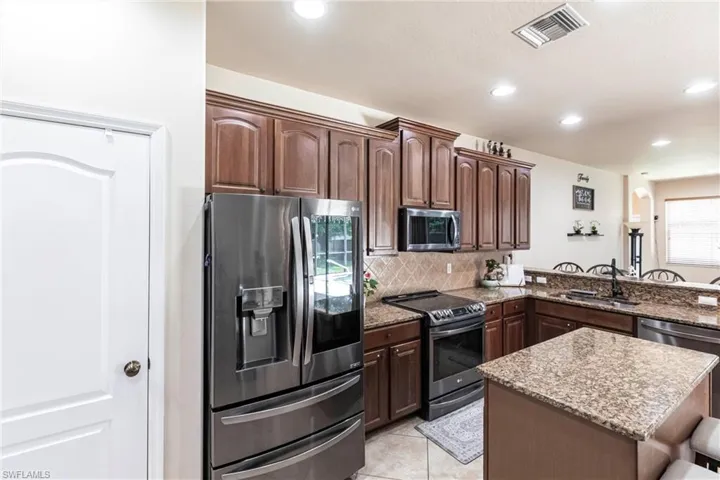 Kitchen featuring light stone counters, a sink, stainless steel appliances, decorative backsplash, and visible vents