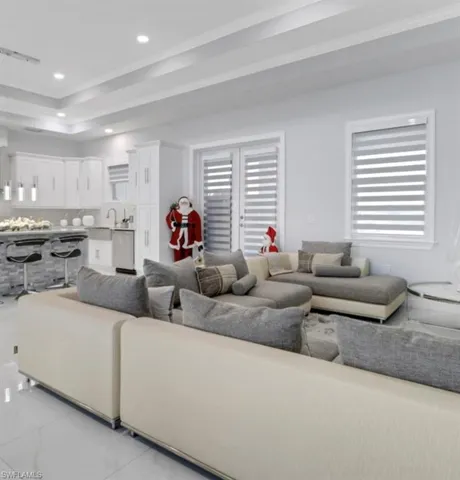 Living room featuring crown molding, light marble finish flooring, a tray ceiling, recessed lighting, and plenty of natural light