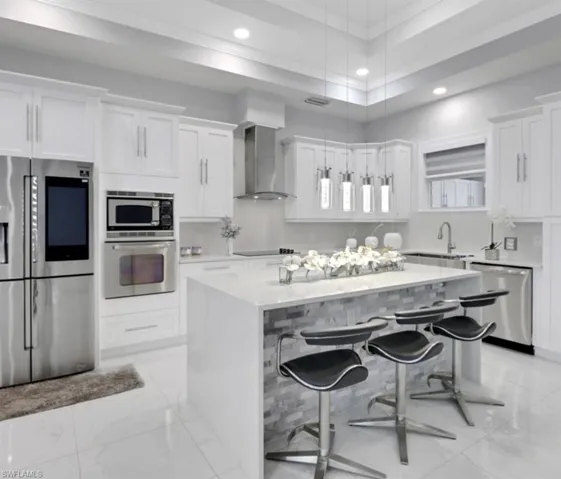 Kitchen with stainless steel appliances, a kitchen island, white cabinetry, wall chimney range hood, and recessed lighting