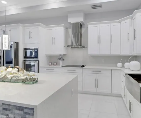 Kitchen with stainless steel appliances, white cabinets, wall chimney range hood, crown molding, and decorative light fixtures