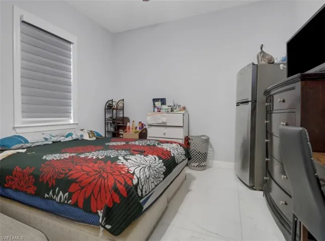 Bedroom featuring freestanding refrigerator and light marble finish floors