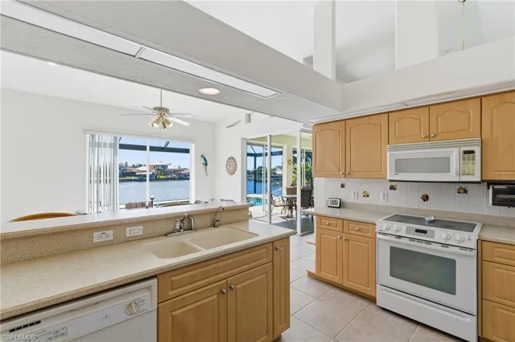 Kitchen featuring white appliances, backsplash, light tile patterned floors, light wood finish cabinets, and light stone counters