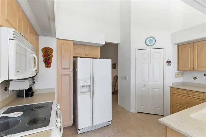 Kitchen with white appliances, light wood finish cabinetry, light tile patterned flooring, backsplash, and a high ceiling