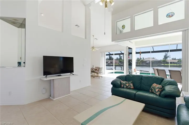 Living room featuring ceiling fan, a sunroom, light tile patterned flooring, and a high ceiling