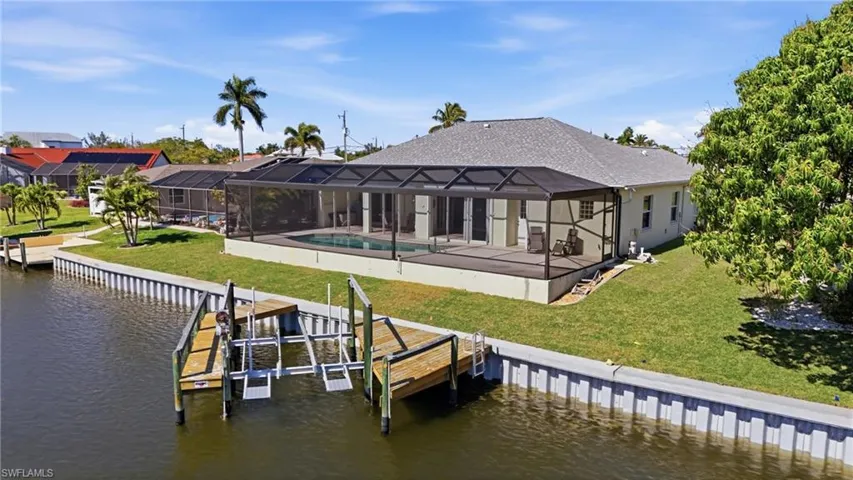 Rear view of house with boat lift, a lawn, a water view, and a lanai