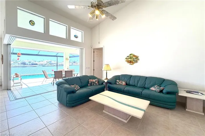 Tiled living area with a sunroom, a ceiling fan, a water view, and vaulted ceiling
