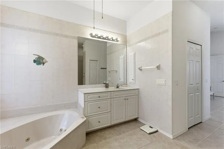 Bathroom with vanity, a whirlpool tub, light tile patterned floors, a closet, and tile walls
