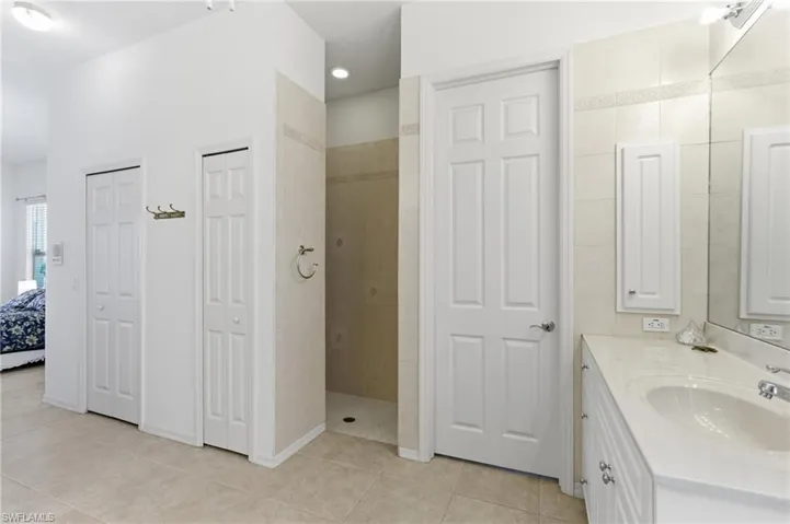 Ensuite bathroom featuring a closet, vanity, light tile patterned floors, and walk in shower