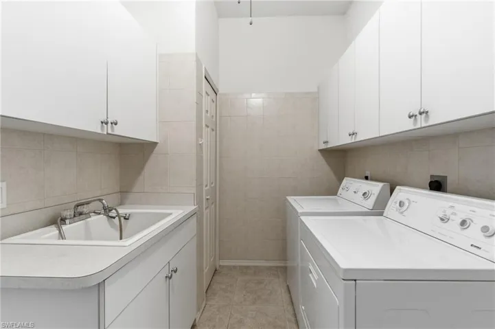 Laundry area featuring cabinet space, washing machine and clothes dryer, light tile patterned floors, and tile walls