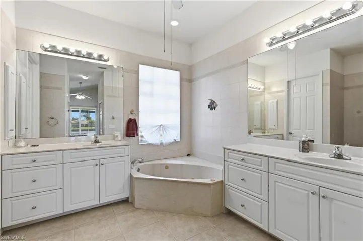 Full bath with two vanities, a ceiling fan, a garden tub, and light tile patterned floors