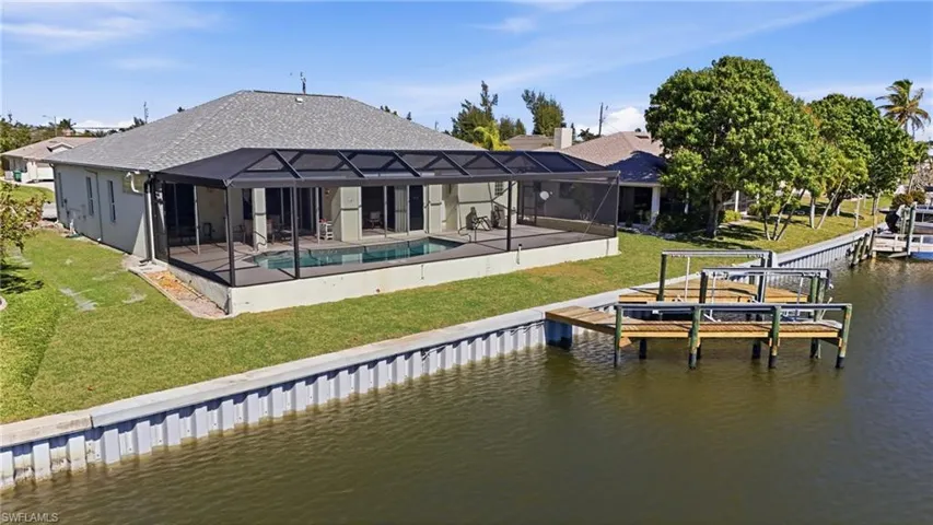 Rear view of property featuring a yard, a sunroom, a water view, a patio area, and glass enclosure