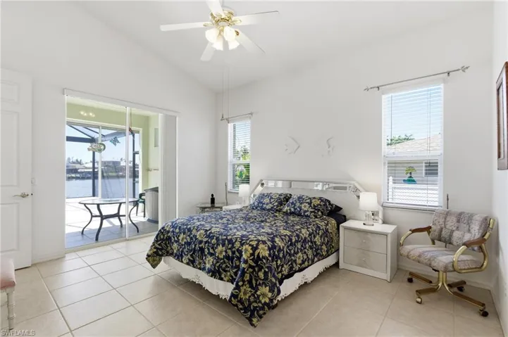 Bedroom with vaulted ceiling, access to exterior, a ceiling fan, light tile patterned flooring, and multiple windows