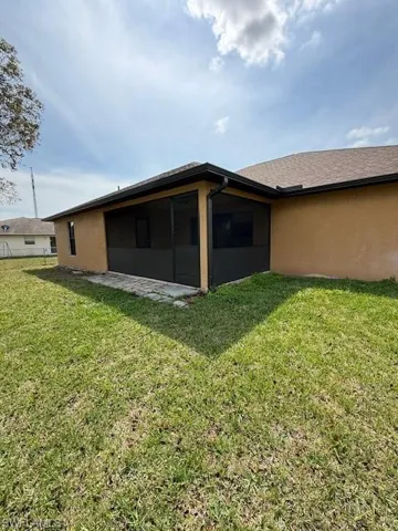 Rear view of house featuring a lawn, a sunroom, and stucco siding