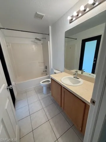 Bathroom featuring vanity, shower / tub combination, a textured ceiling, light tile patterned floors, and a textured wall