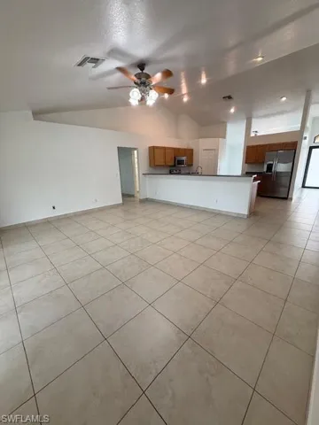 Kitchen featuring open floor plan, dark countertops, wood finish cabinetry, vaulted ceiling, and fridge