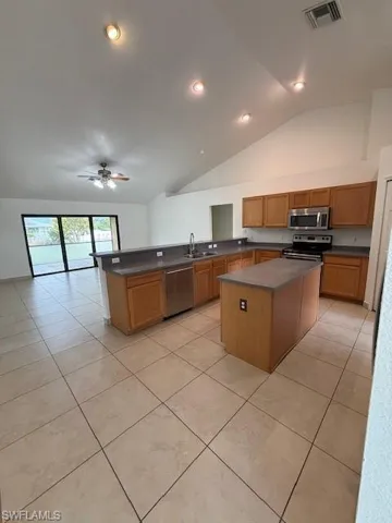 Kitchen featuring a center island, a peninsula, lofted ceiling, a ceiling fan, and stove