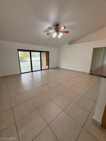 Empty room with a ceiling fan, vaulted ceiling, and light tile patterned floors