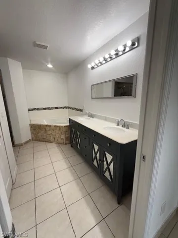 Full bath with double vanity, a bath, light tile patterned floors, and a textured ceiling