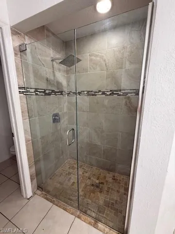Full bath featuring a stall shower, light tile patterned floors, and a textured wall