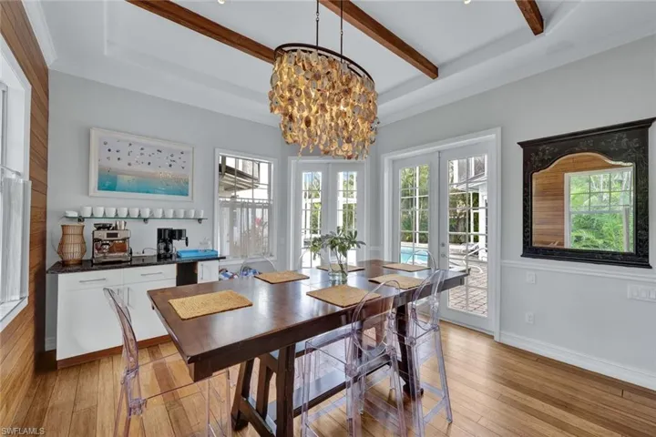 Dining space with beam ceiling, an inviting chandelier, light hardwood / wood-style flooring, ornamental molding, and french doors