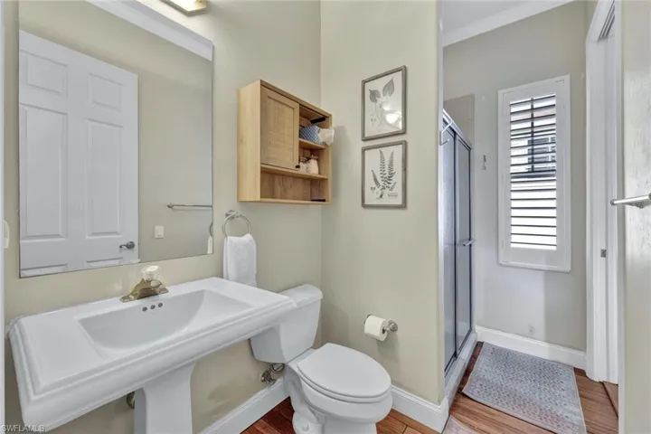 Bathroom with toilet, hardwood / wood-style floors, walk in shower, crown molding, and sink