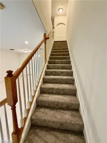 Carpeted staircase featuring a wood handrail with white balusters