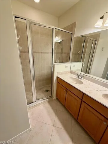 Bathroom featuring a glass-enclosed shower with tile surround, a dual vanity with light-colored countertops, and wood-finish cabinetry