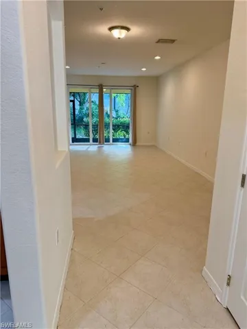 Spacious living area featuring neutral-toned tile flooring, recessed lighting, and a prominent sliding glass door leading to an outdoor space
