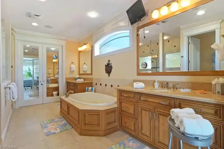 Ensuite bathroom with healthy amount of natural light, a garden tub, vanity, french doors, and crown molding