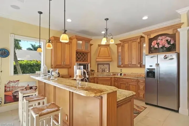 Kitchen with stainless steel refrigerator with ice dispenser, a peninsula, glass insert cabinets, a kitchen breakfast bar, and light stone countertops