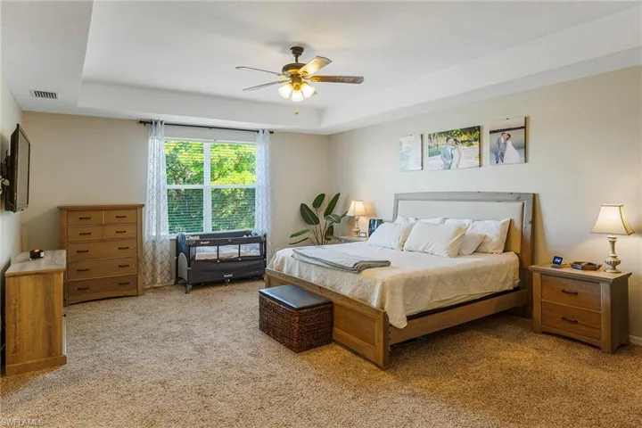 Carpeted bedroom with ceiling fan and a tray ceiling