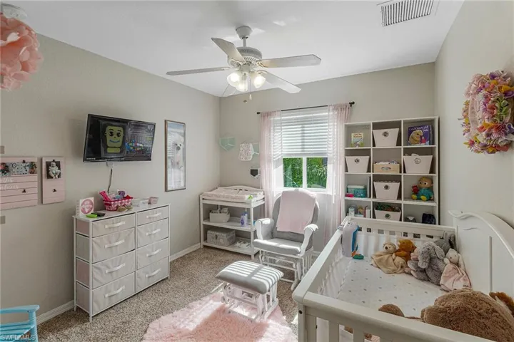 Carpeted bedroom featuring a crib and ceiling fan