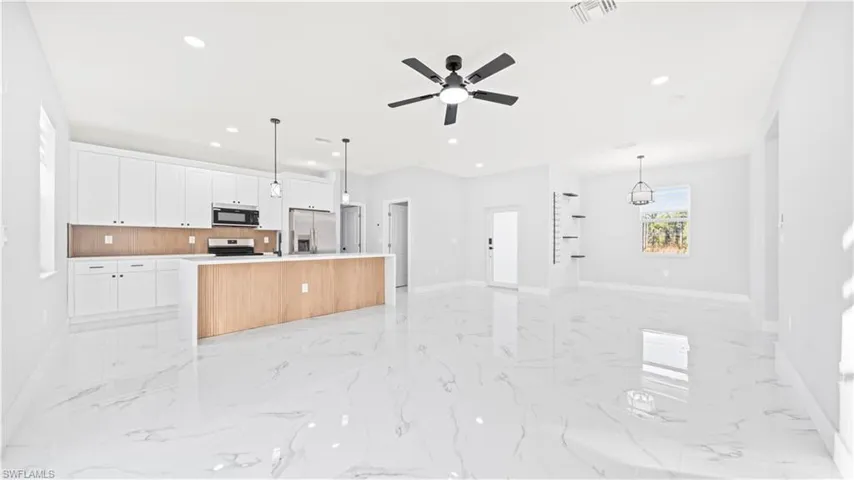 Kitchen featuring open floor plan, an island with sink, white cabinetry, hanging light fixtures, and light marble finish floors
