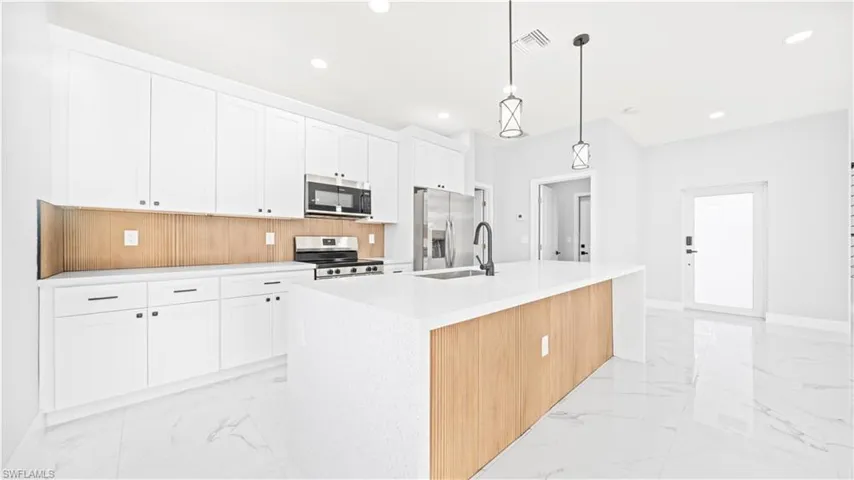 Kitchen featuring white cabinetry, light marble finish flooring, stainless steel appliances, a kitchen island with sink, and recessed lighting