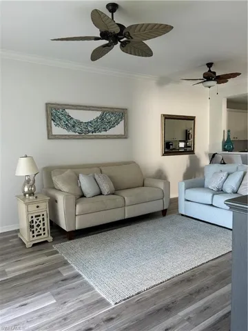 Living room featuring wood-type flooring, crown molding, and ceiling fan