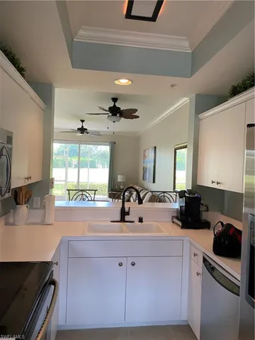 Kitchen with white cabinetry, dishwashing machine, sink, ceiling fan, and a raised ceiling