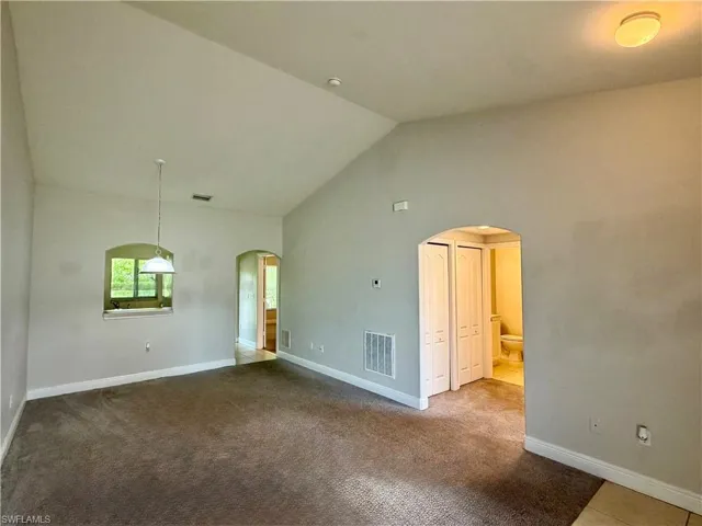 Spacious room featuring vaulted ceilings, neutral-toned walls, and dark carpeting