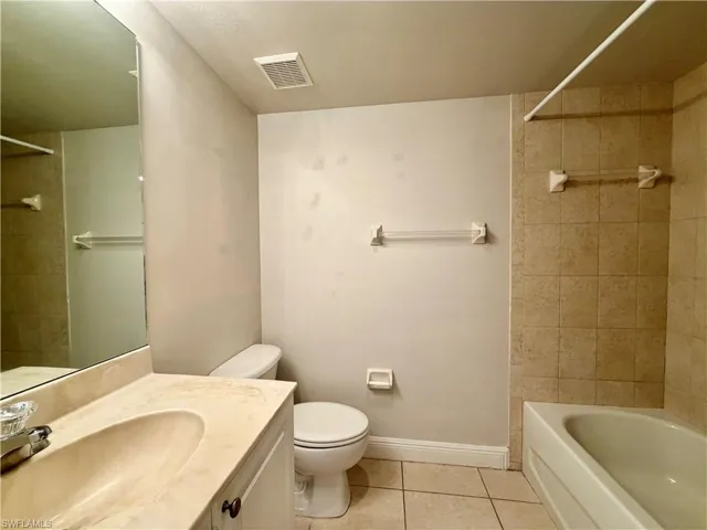 Bathroom featuring a full vanity with an integrated sink, a rectangular mirror, a bathtub with tiled surround, and tiled flooring