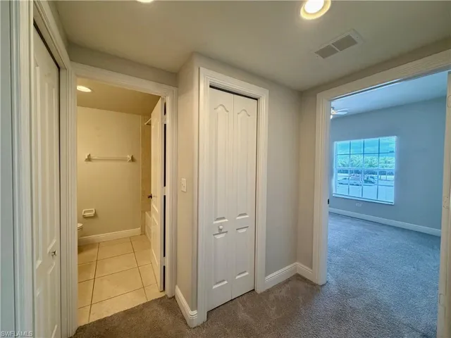 Interior hallway featuring recessed ceiling lighting, a bathroom with tile flooring and a built-in tub, and a bedroom with carpeting and a window