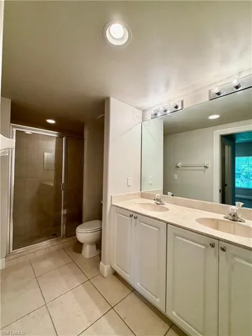 Bathroom featuring a dual-sink vanity with light-toned countertops, white cabinetry, a large mirror, a glass-enclosed shower with tiled walls, and recessed lighting