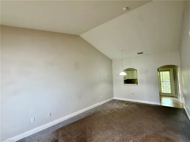 Living area featuring vaulted ceilings, textured carpeting, and a pendant light fixture