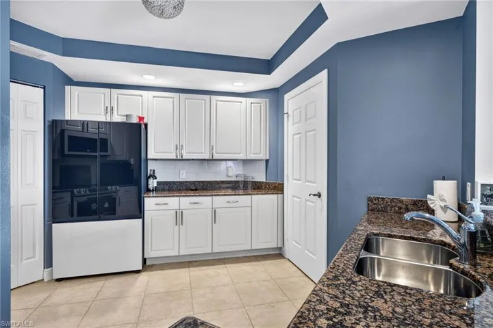 Kitchen with refrigerator, white cabinets, dark stone counters, light tile patterned floors, and recessed lighting